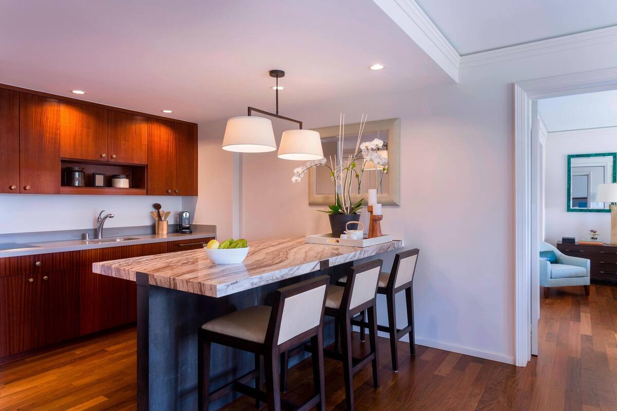 A modern kitchen with wooden cabinets, a marble island, and bar stools.