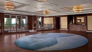 A spacious room with a large blue carpet, wooden flooring, and a balcony with a railing.