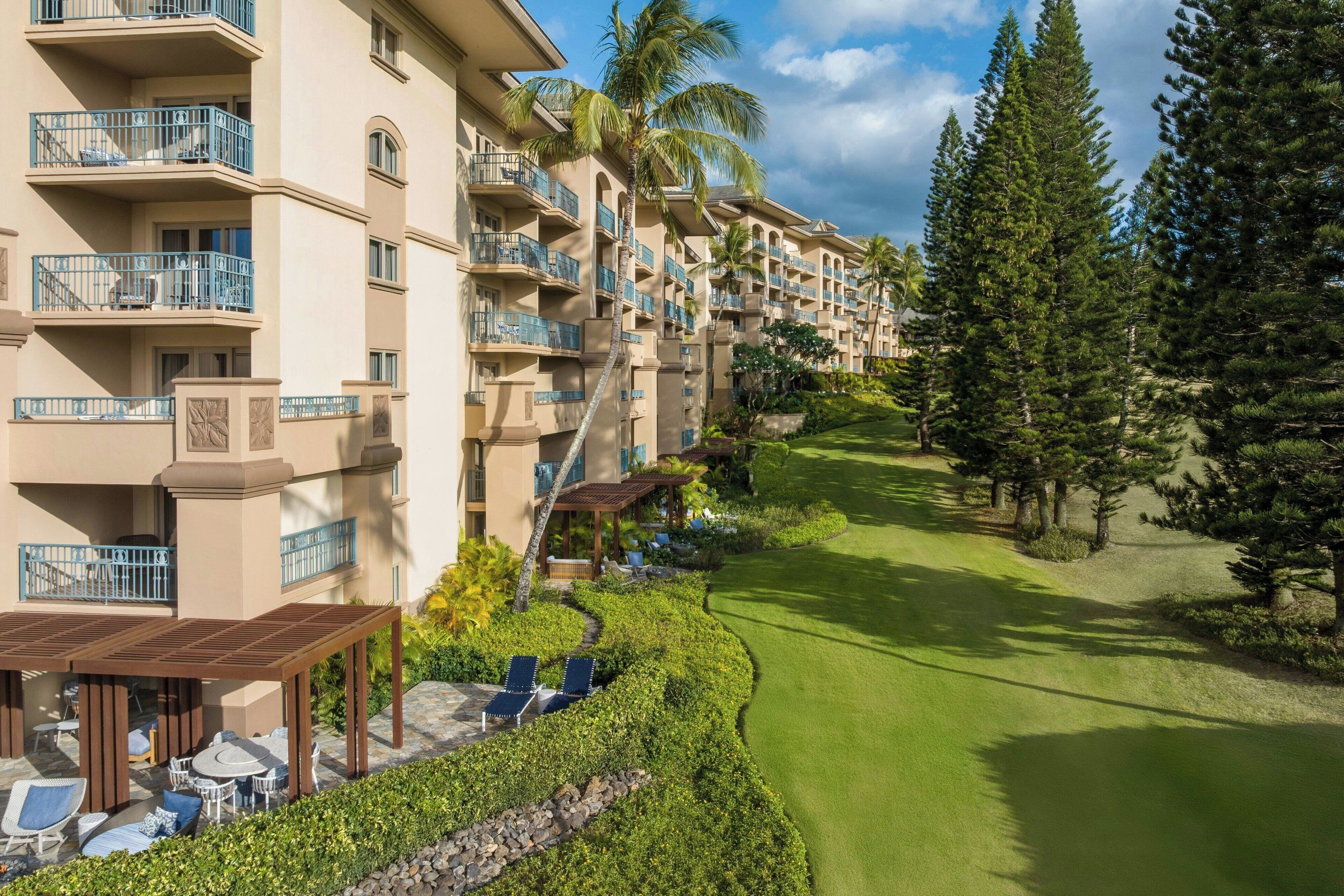 A multi-story hotel with balconies, a covered outdoor seating area, and a well-maintained lawn.