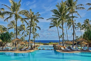 A pool area with lounge chairs and palm trees, overlooking the ocean.