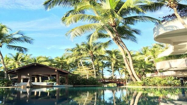 A clear view of a swimming pool surrounded by palm trees and a building with a covered patio area. - ParkCity Everly Hotel Miri (Miri)