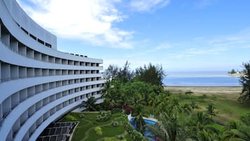 A modern hotel with a curved facade, a pool, and a view of the beach.