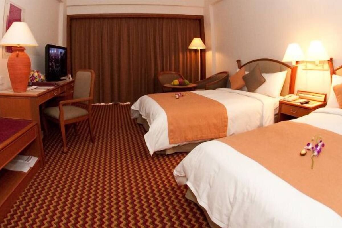 Habitació d'hotel amb dos llits, una taula de treball amb cadira, televisió i un gran finestral amb cortines.