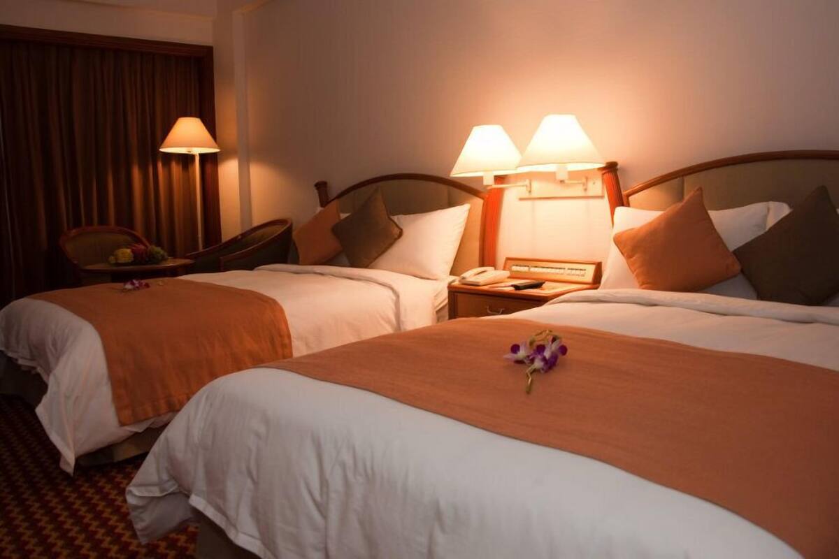 Habitació d'hotel amb dos llits, cada un amb un edredó marró i roba de llit blanca. Hi ha dues làmpades de nit, una cadira i una taula petita amb una làmpada.