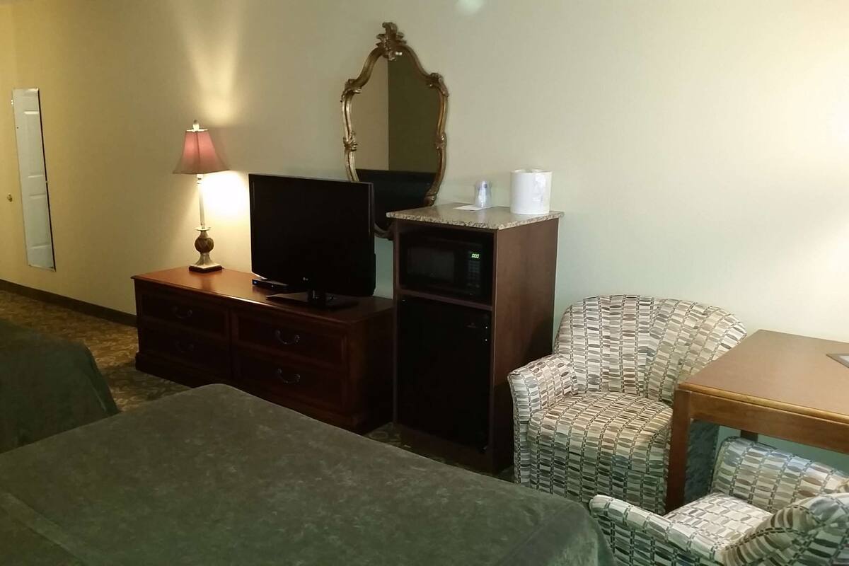 A hotel room with two beds, a TV, a dresser, a microwave, a patterned armchair, and a small table.