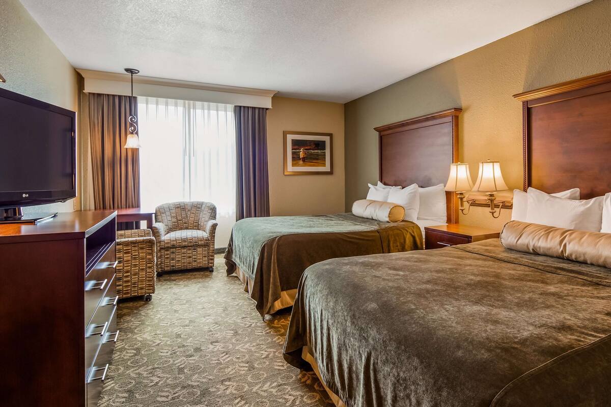 A hotel room with two beds, a TV, a chair, a desk, and a window with curtains.