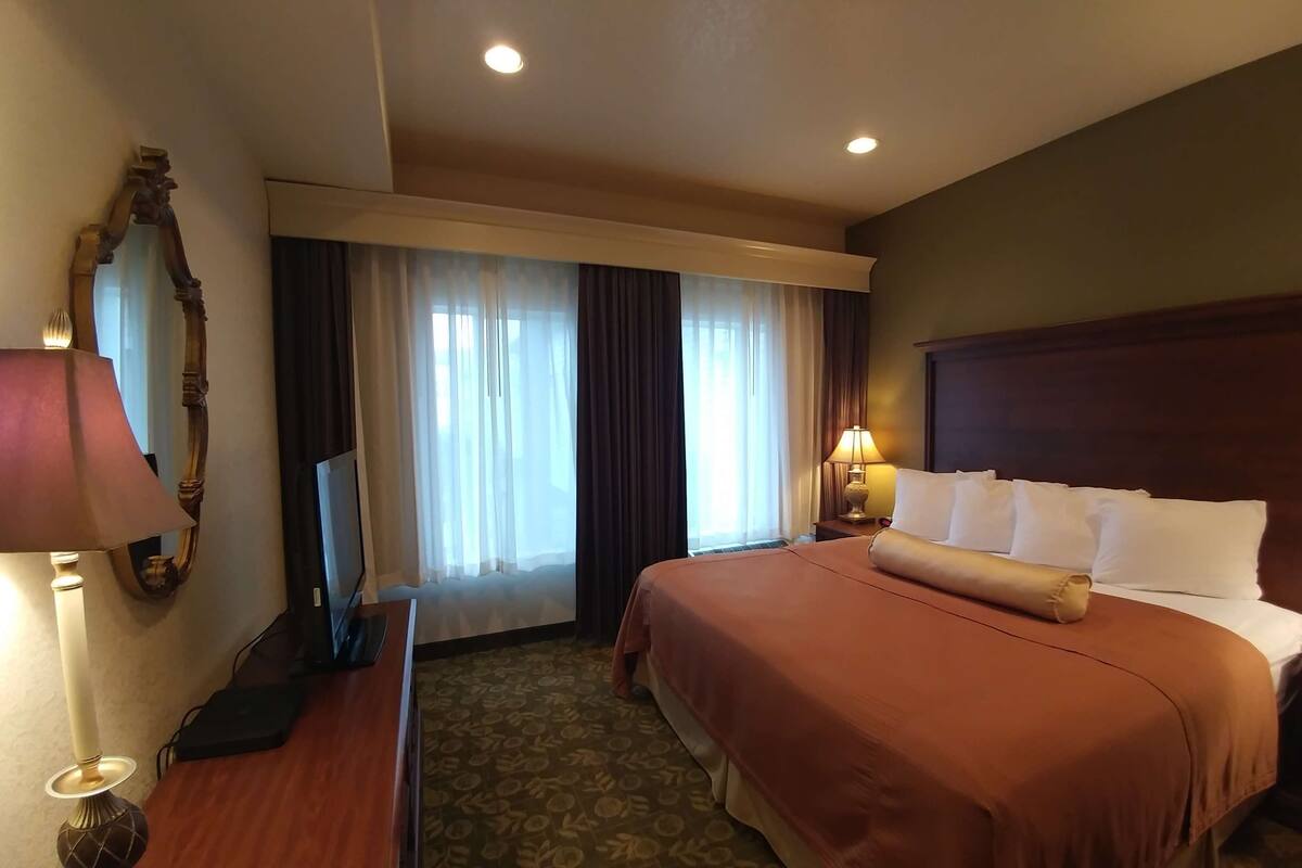 A hotel room with a large bed, a desk with a lamp, a television, and a mirror.