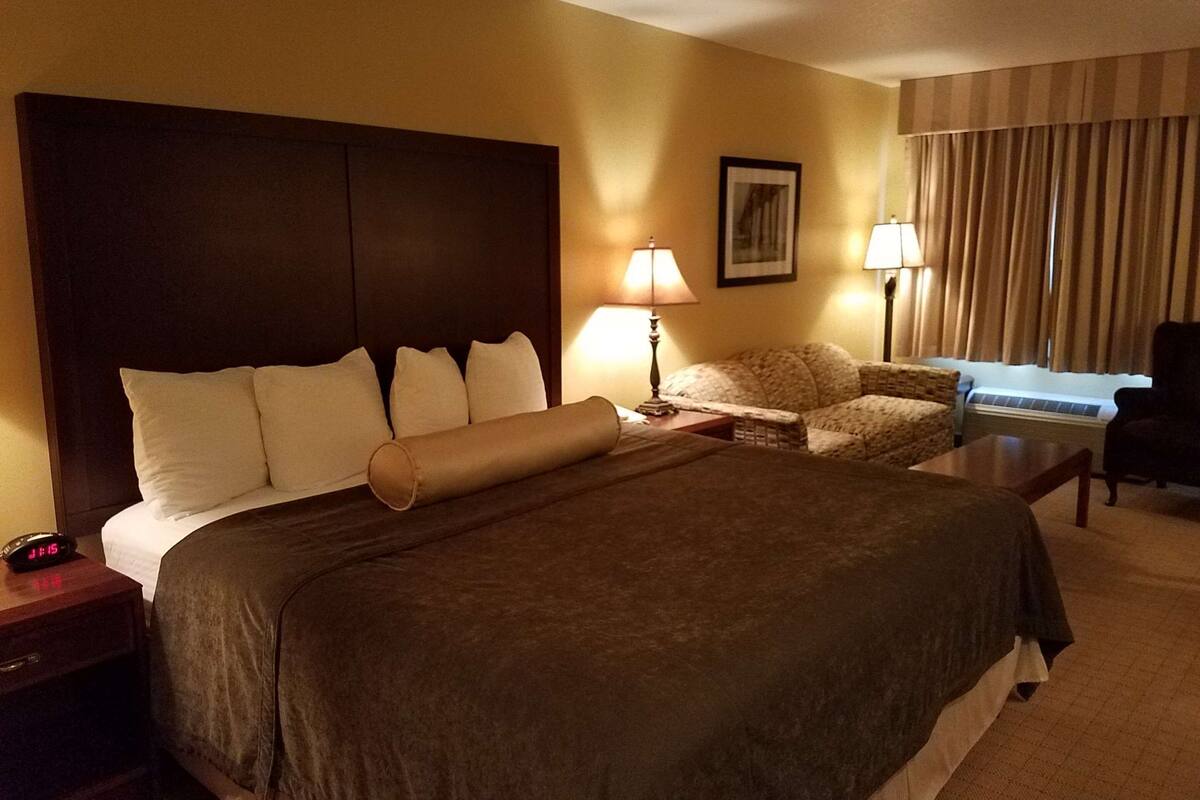 A hotel room with a large bed, two bedside tables, a chair, a desk, and a window with curtains.