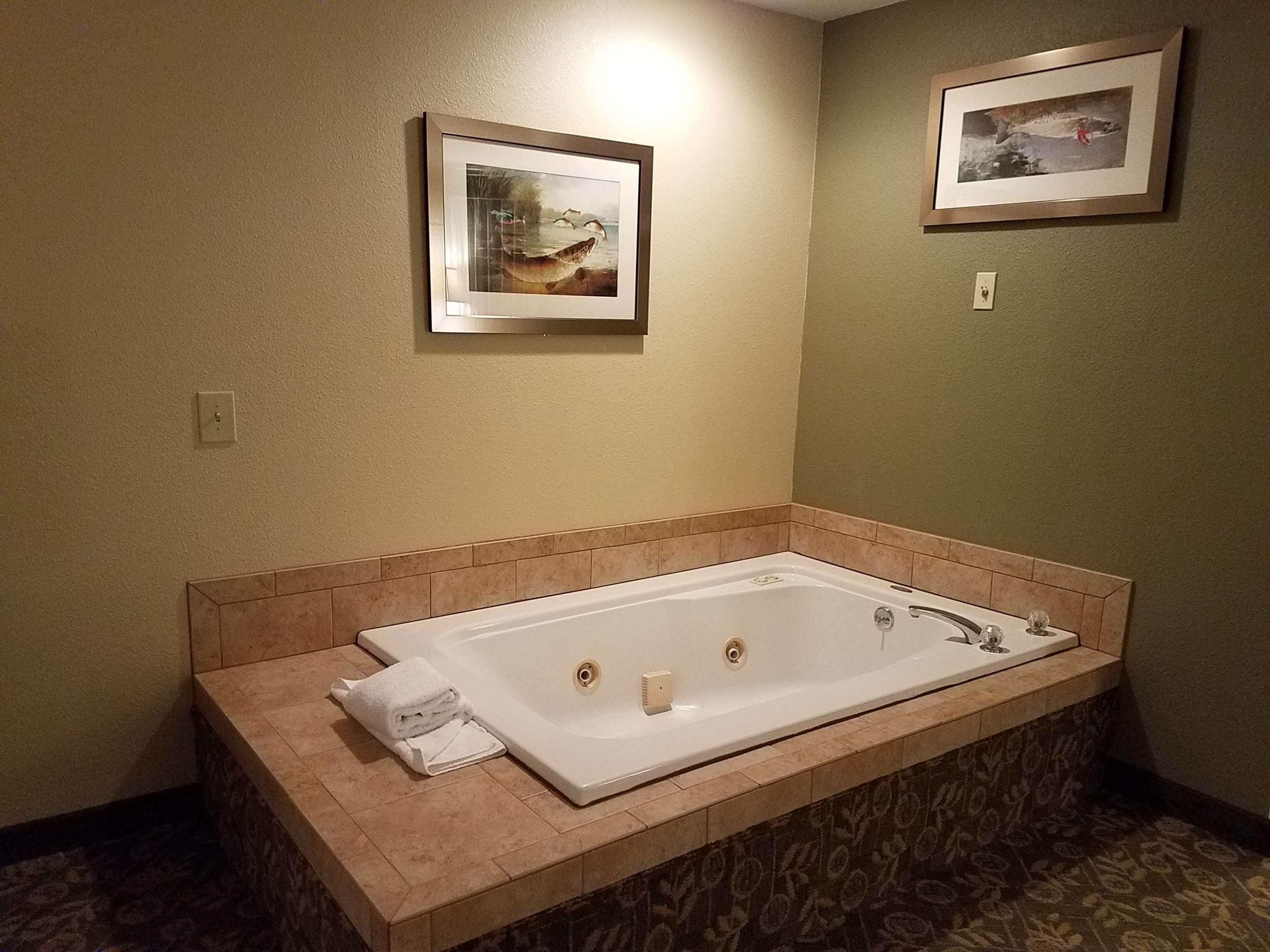 Un baño con una bañera rectangular grande, paredes color beige y dos cuadros enmarcados.