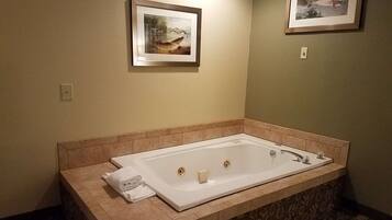 Un baño con una bañera rectangular grande, paredes color beige y dos cuadros enmarcados.