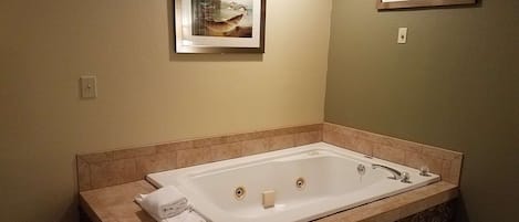 A bathroom with a large rectangular bathtub, beige walls, and two framed pictures on the walls.
