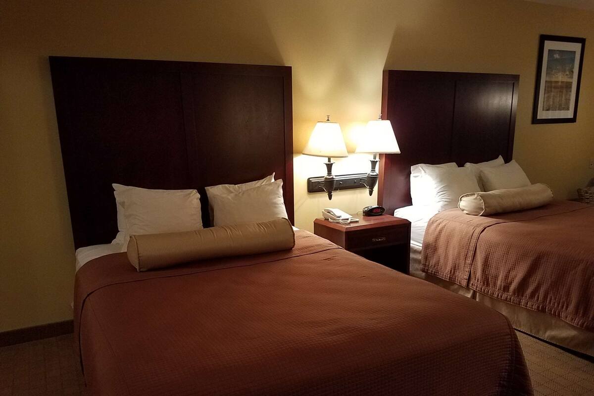 A hotel room with two beds, each with a headboard, a nightstand with a lamp, and a framed picture on the wall.
