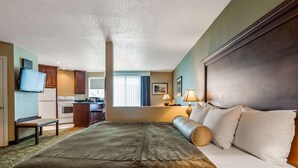A hotel room with a bed, a desk, a kitchenette, and a television.