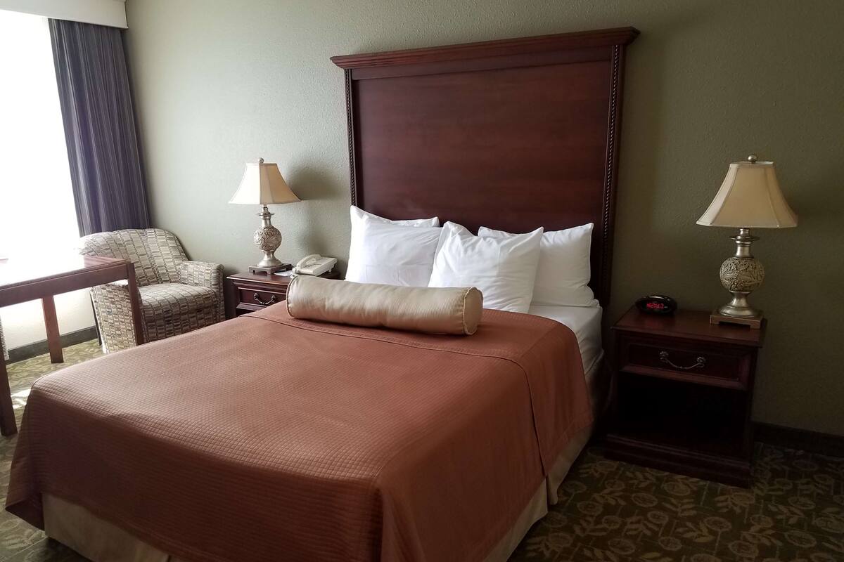 A hotel room with a large bed, two bedside tables, a chair, and a lamp on each side of the bed.