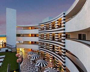 A multi-level hotel with a curved exterior, outdoor seating area with umbrellas, and a checkered floor pattern. - Carlyle Inn (Los Angeles)