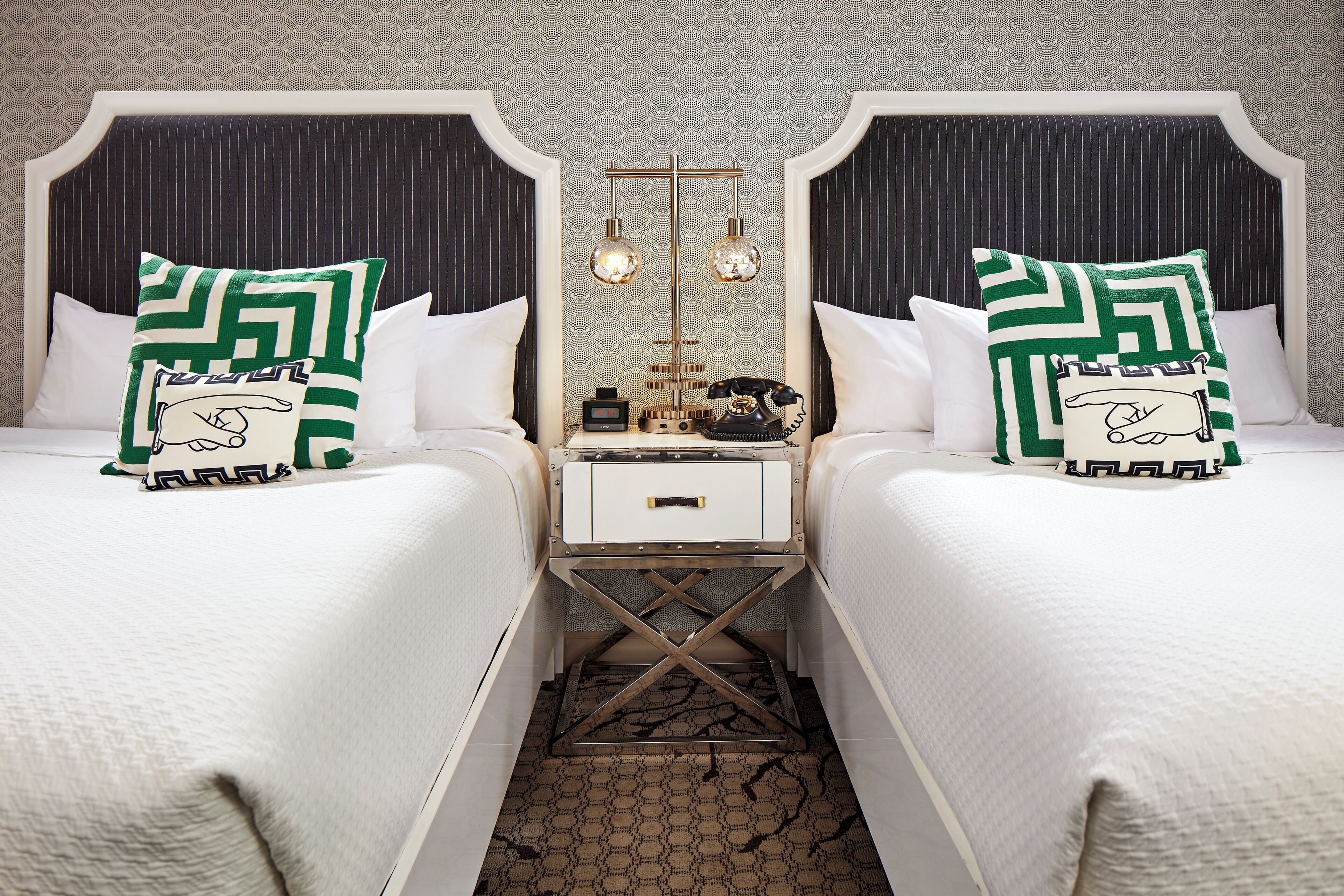 A hotel room with two beds, a nightstand with a telephone, and a mirror above the nightstand.