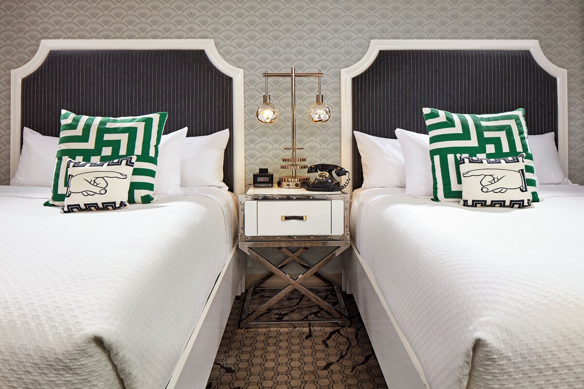 A hotel room with two beds, a nightstand with a telephone, and a mirror above the nightstand.