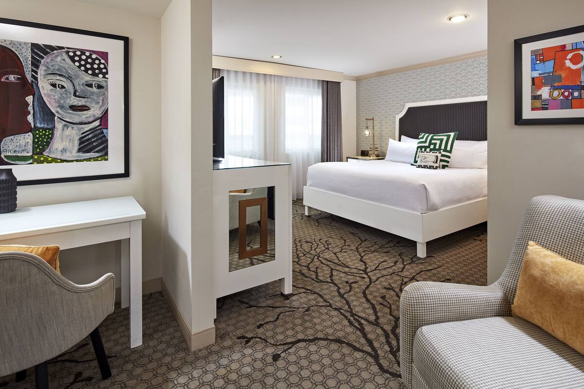 A hotel room with a bed, a desk, a chair, and artwork on the walls.