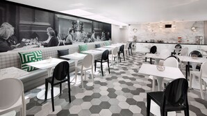 Un restaurante moderno con suelo de patrón hexagonal, sillas blancas y negras, y un gran ventanal que muestra una fotografía blanco y negro de personas cenando.