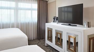 A hotel room with two beds, a television on a white cabinet, and a coffee machine.