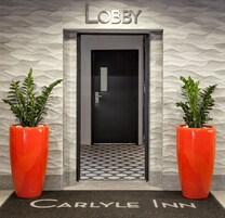 A lobby entrance with a textured wall, a door labeled "Lobby", and two potted plants.