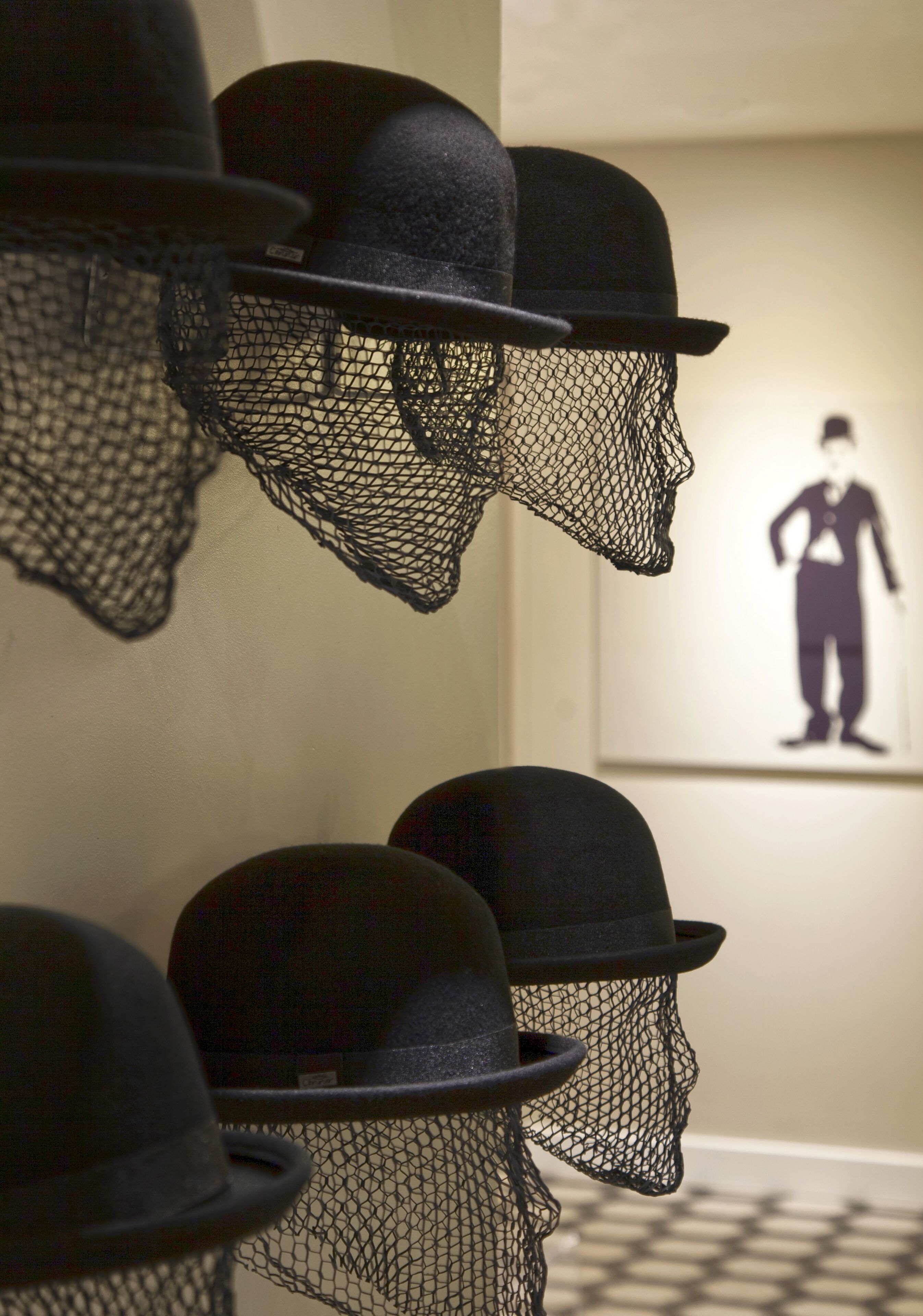 A wall with multiple black hats and a silhouette of a person.