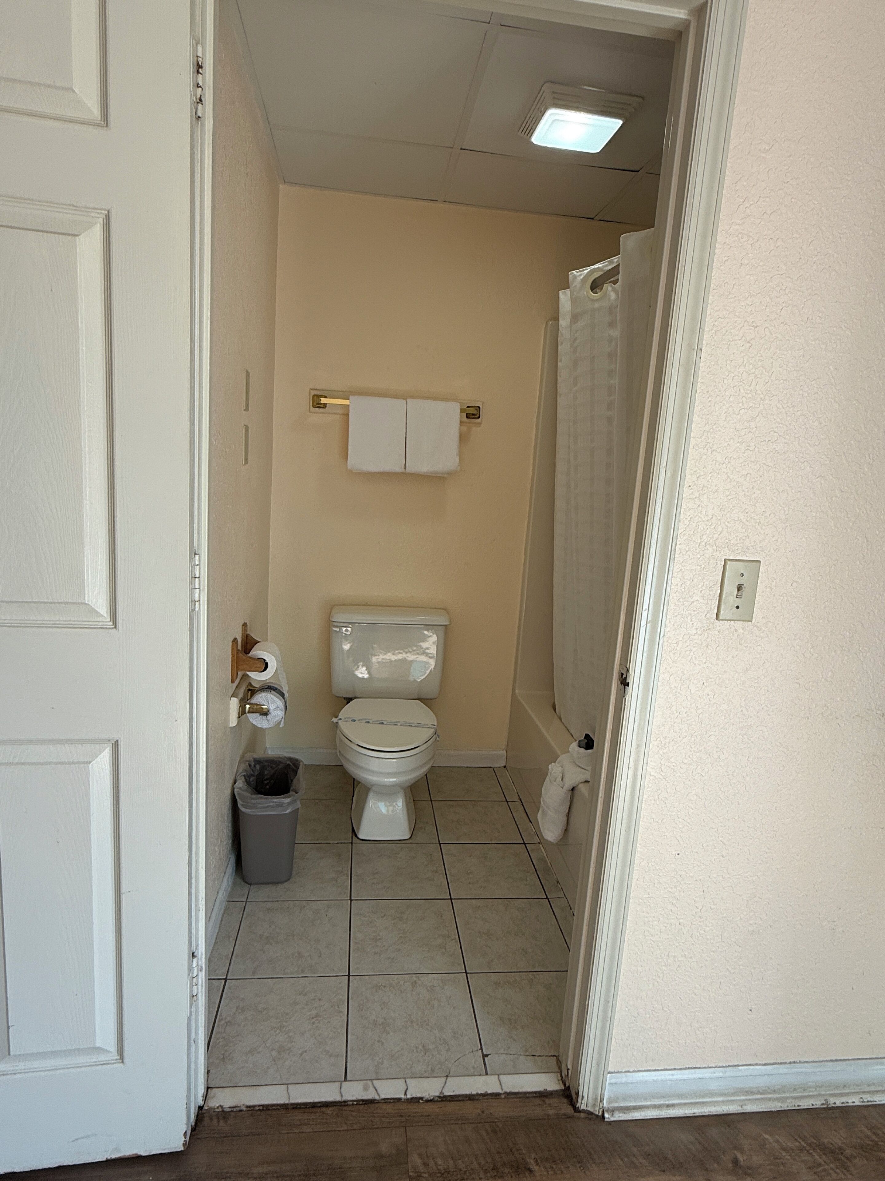 Une petite salle de bain propre, équipée de toilettes, d’une poubelle et d’un porte-serviettes.