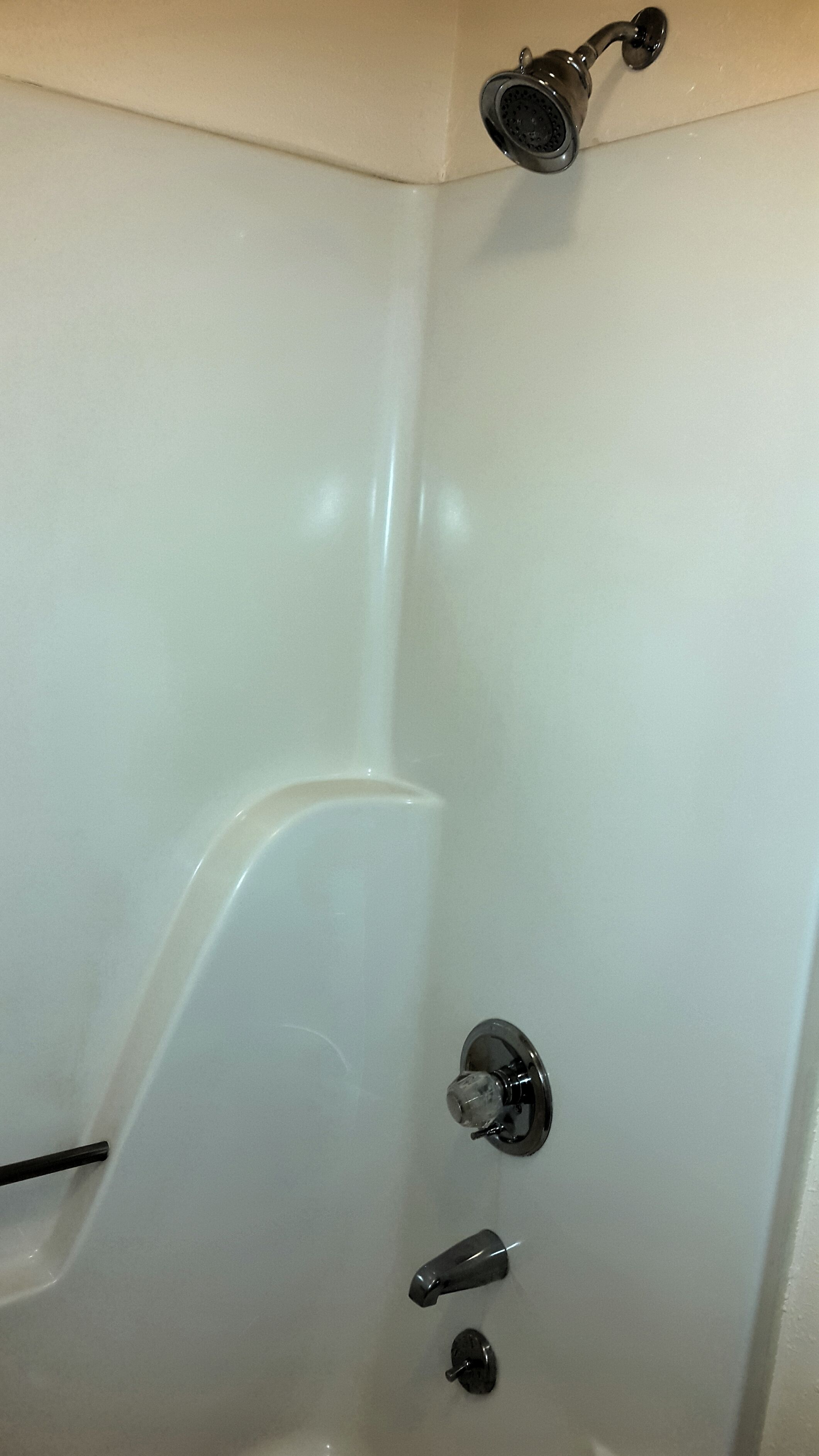 A white shower with a handheld showerhead, a wall-mounted faucet, and a control knob.
