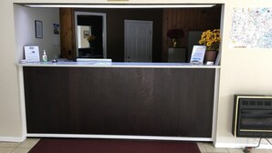 Un mostrador de recepción con acabado de madera oscura, una alfombra roja, una impresión enmarcadas de motivos botánicos y un mapa en la pared.