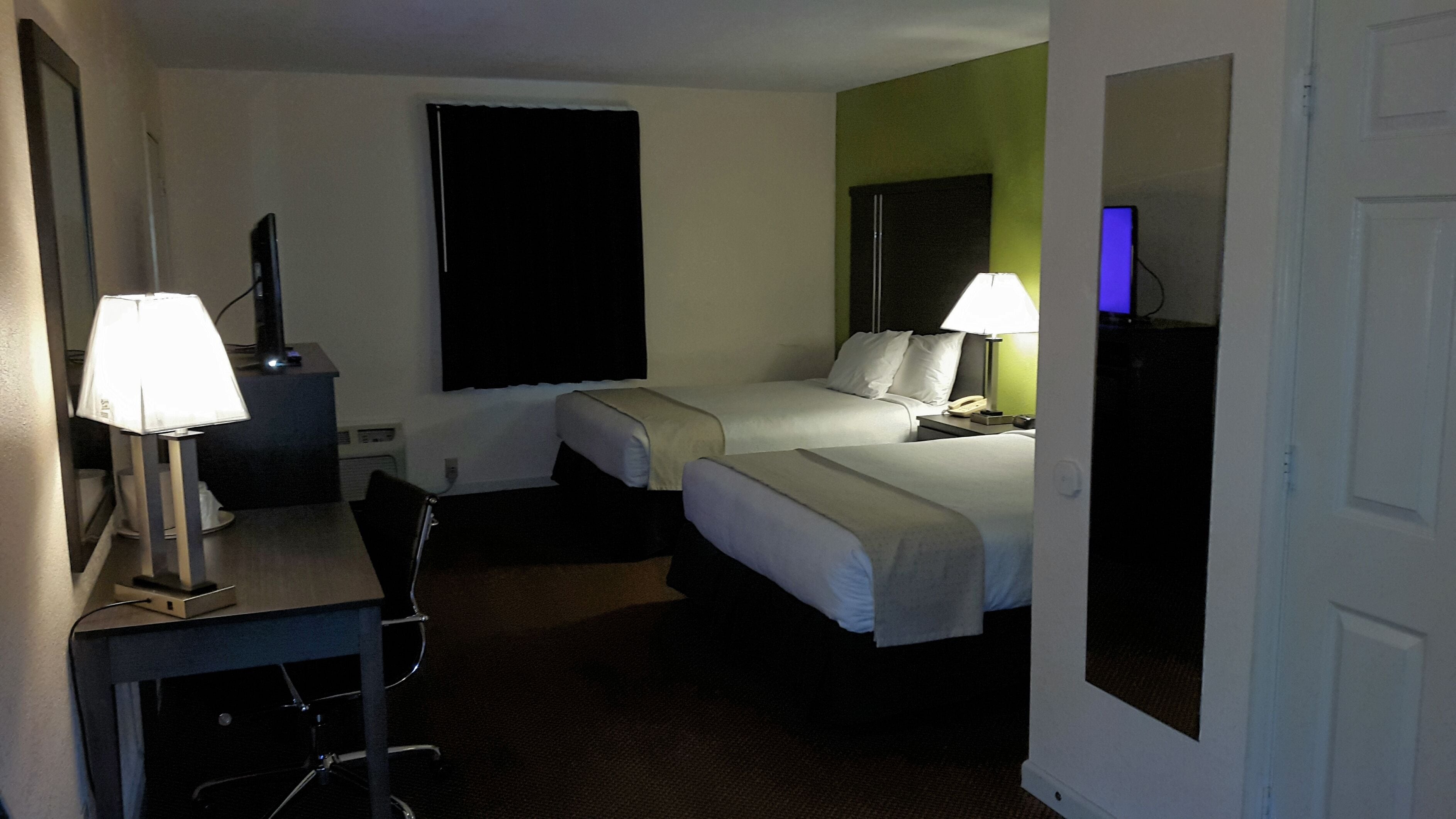 A hotel room with two beds, a desk with a lamp, a chair, and a television.