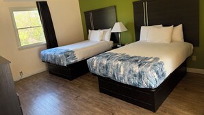Habitación de hotel con dos camas, una ventana con cortinas, una lámpara y suelo de madera.
