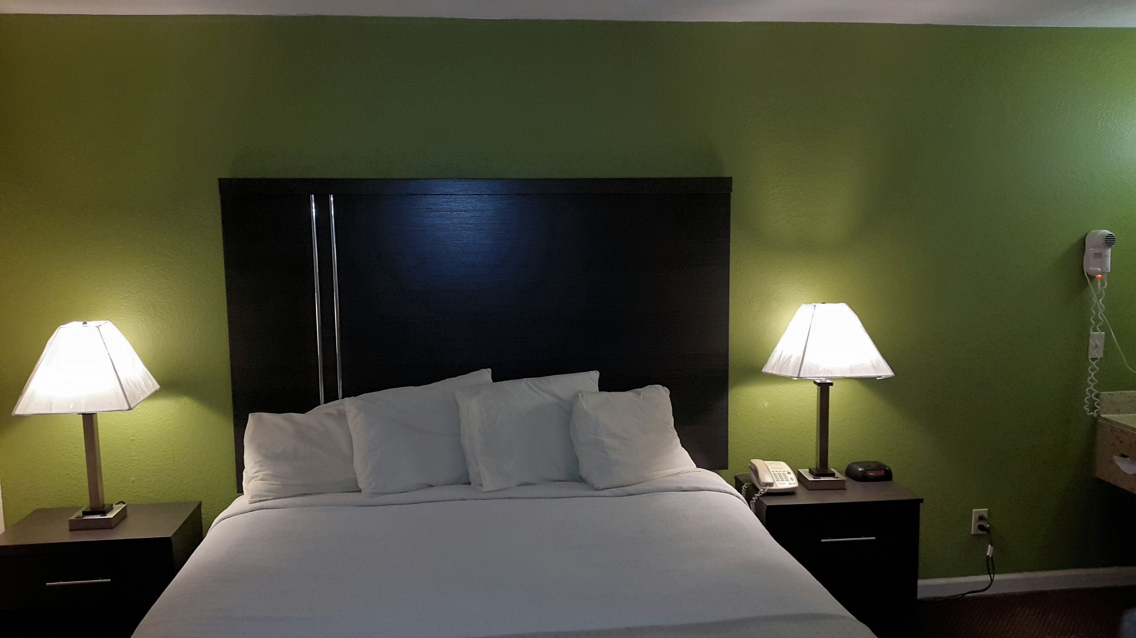 A hotel room with a large bed, two bedside tables, a nightstand, a lamp, a phone, and a wall socket.