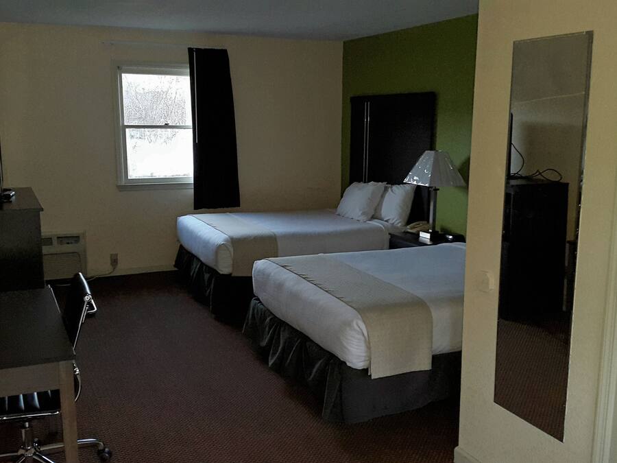 Habitación de hotel con dos camas, un escritorio con lámpara, una silla y una ventana con cortinas.