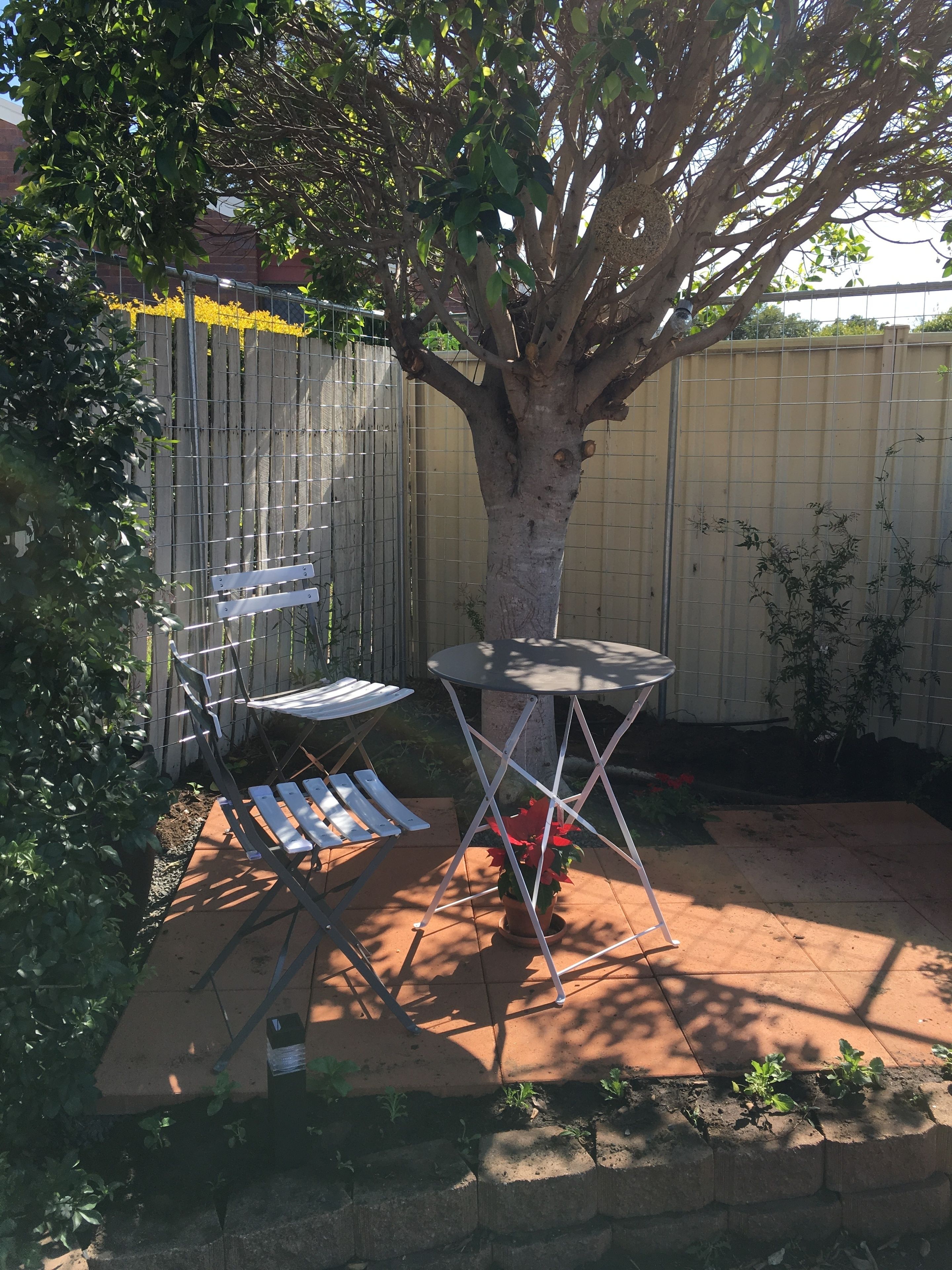 Un jardin avec un arbre, une table en métal et une chaise pliante blanche.