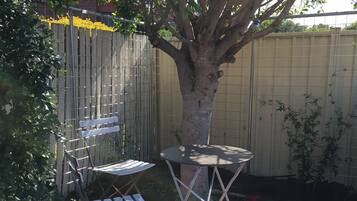Un jardin avec un arbre, une table en métal et une chaise pliante blanche.