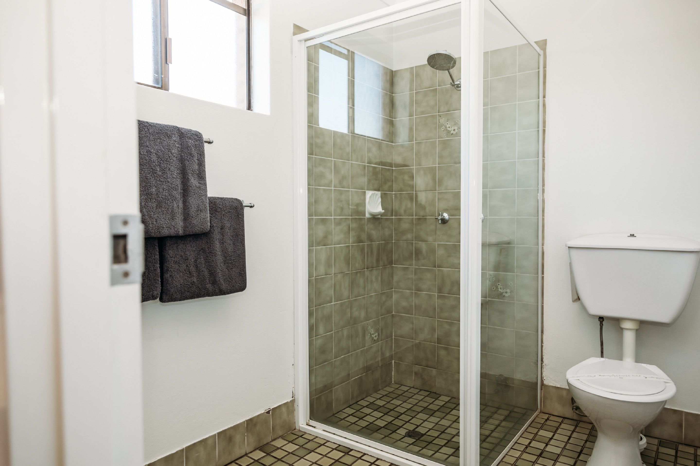 Een badkamer met een douchecabine van glas, een toilet en een handdoekrek met twee handdoeken.