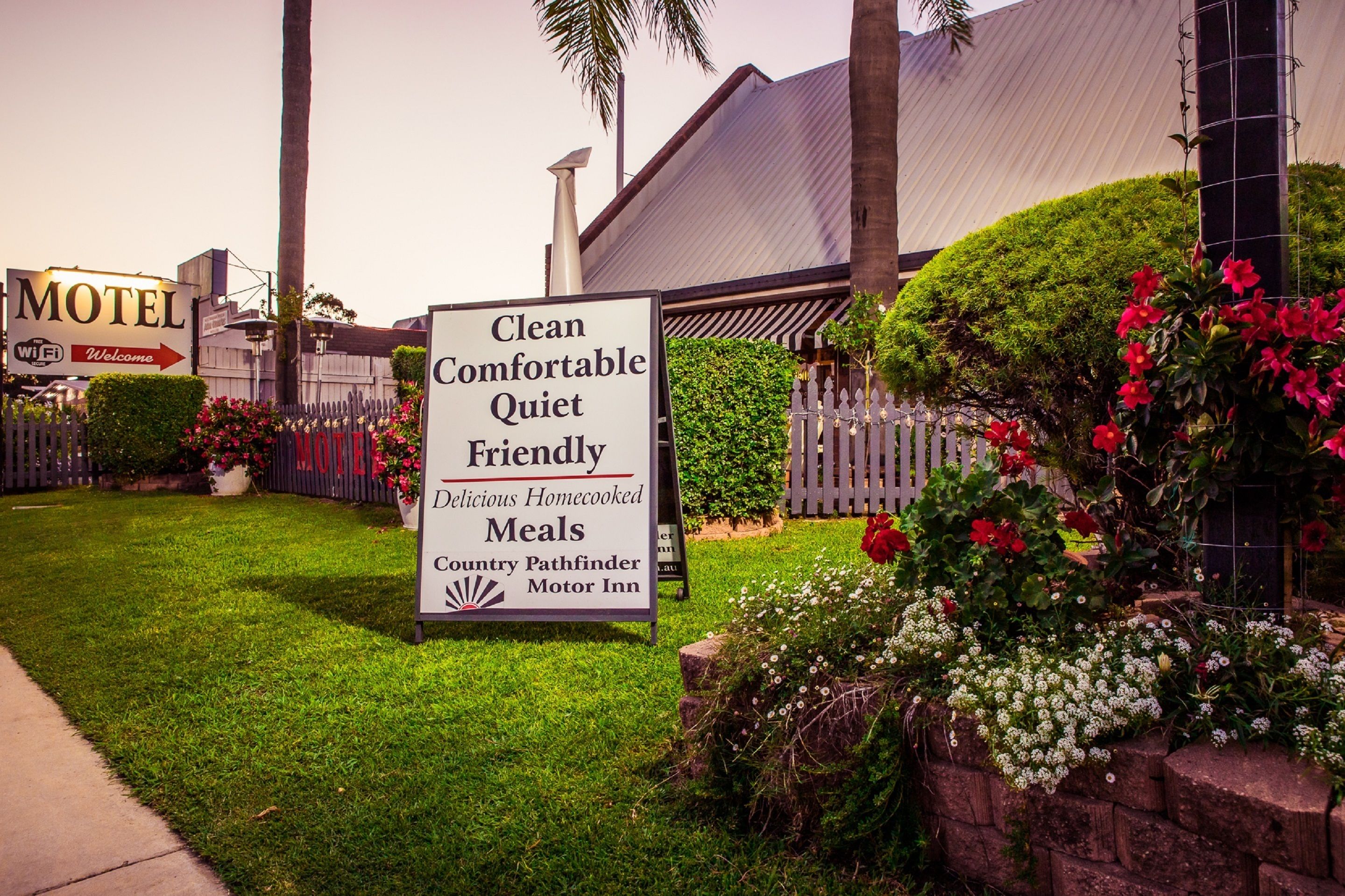 Letrero de motel que anuncia comodidades como limpieza, confort, tranquilidad, atención amable y comidas caseras deliciosas, además de un camino rural.