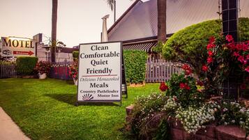 Letrero de motel que anuncia comodidades como limpieza, confort, tranquilidad, atención amable y comidas caseras deliciosas, además de un camino rural.