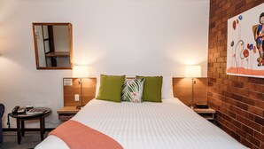 Habitación de hotel con una cama grande, dos lámparas de noche, una mesita con un teléfono, un espejo y una pared de ladrillo con un cuadro.