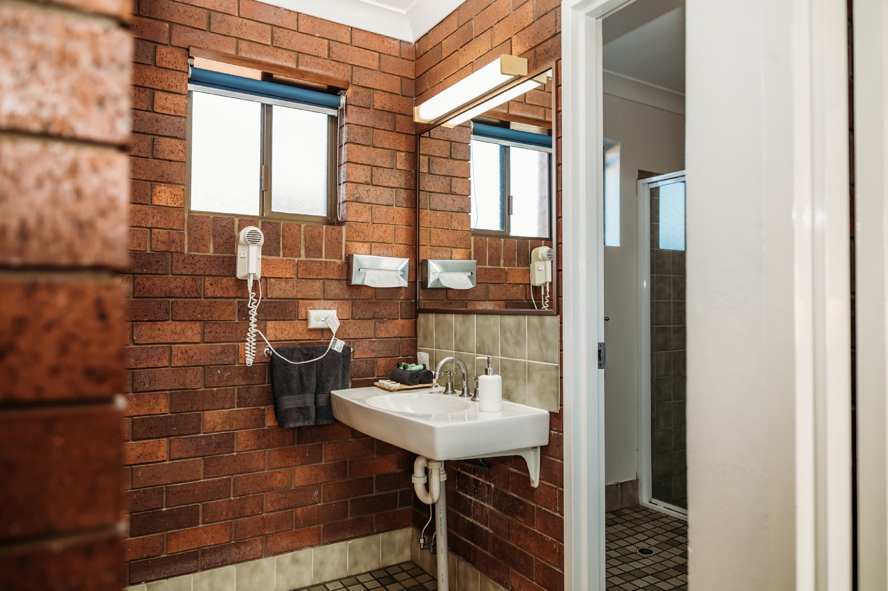 A bathroom with a brick wall, a sink with a mirror, and a window.