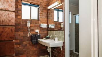 A bathroom with a brick wall, a sink with a mirror, and a window.