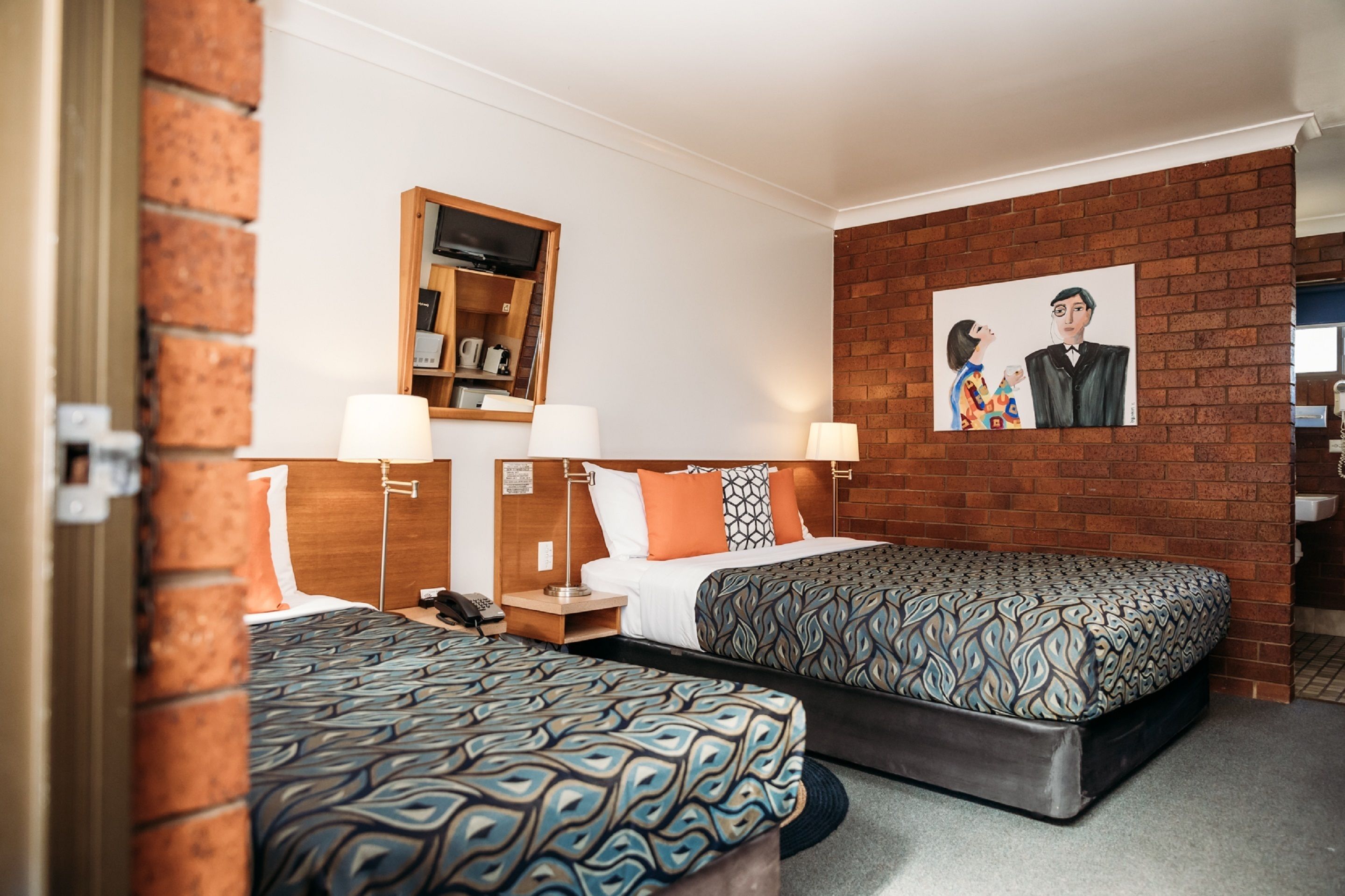 Ein Hotelzimmer mit zwei Betten, einer Ziegelwand, einem Gemälde und einem Holzregal mit Gegenständen.