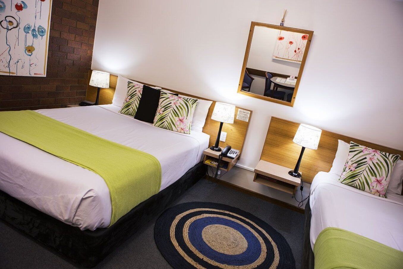 A hotel room with two beds, a desk, a mirror, and a rug.