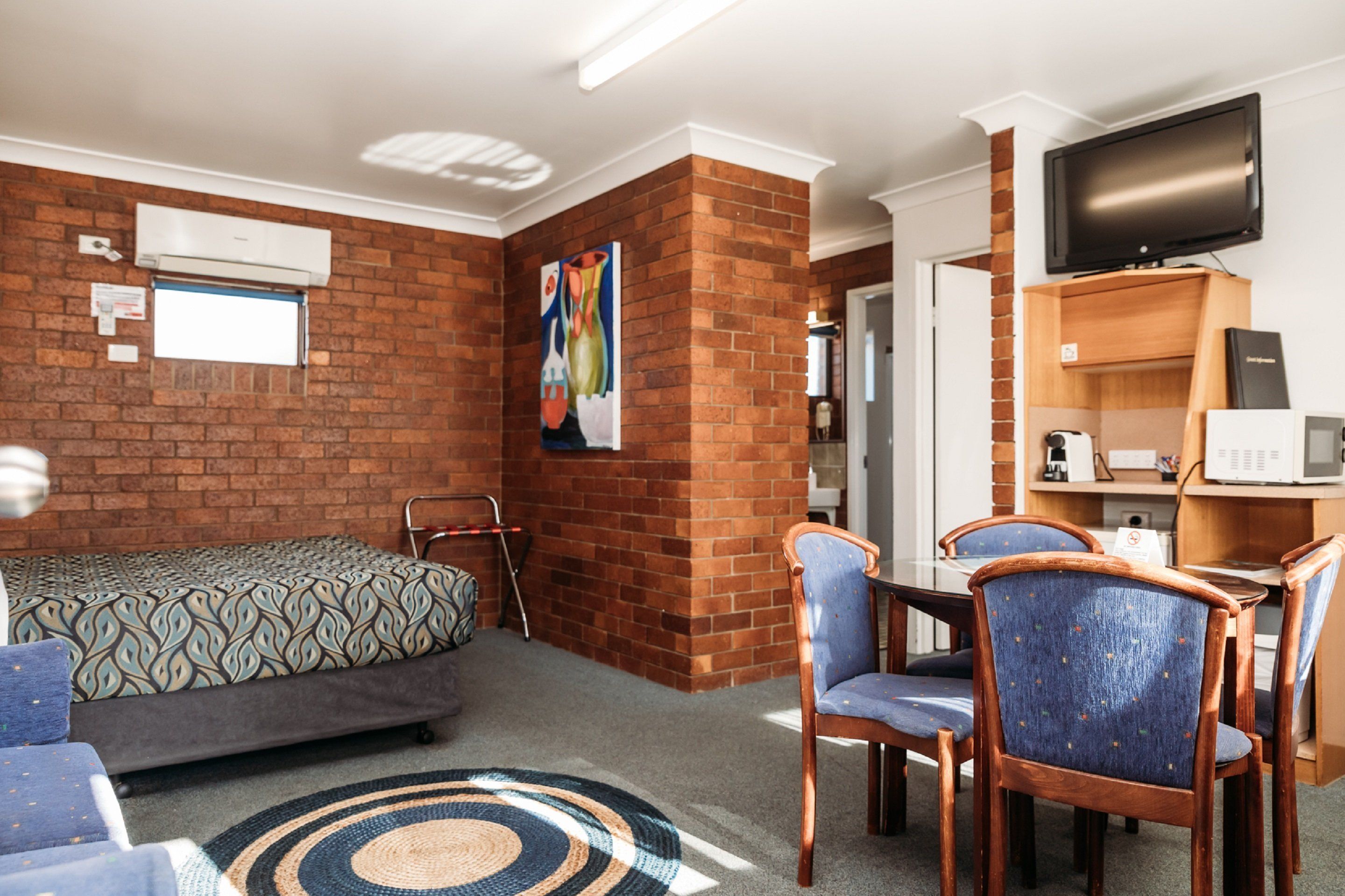 Une chambre d’hôtel avec un mur décoratif en briques, un lit, un bureau avec un ordinateur, une télévision et un coin repas avec des chaises.