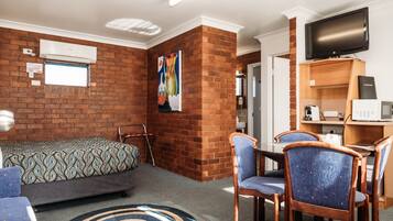Une chambre d’hôtel avec un mur décoratif en briques, un lit, un bureau avec un ordinateur, une télévision et un coin repas avec des chaises.