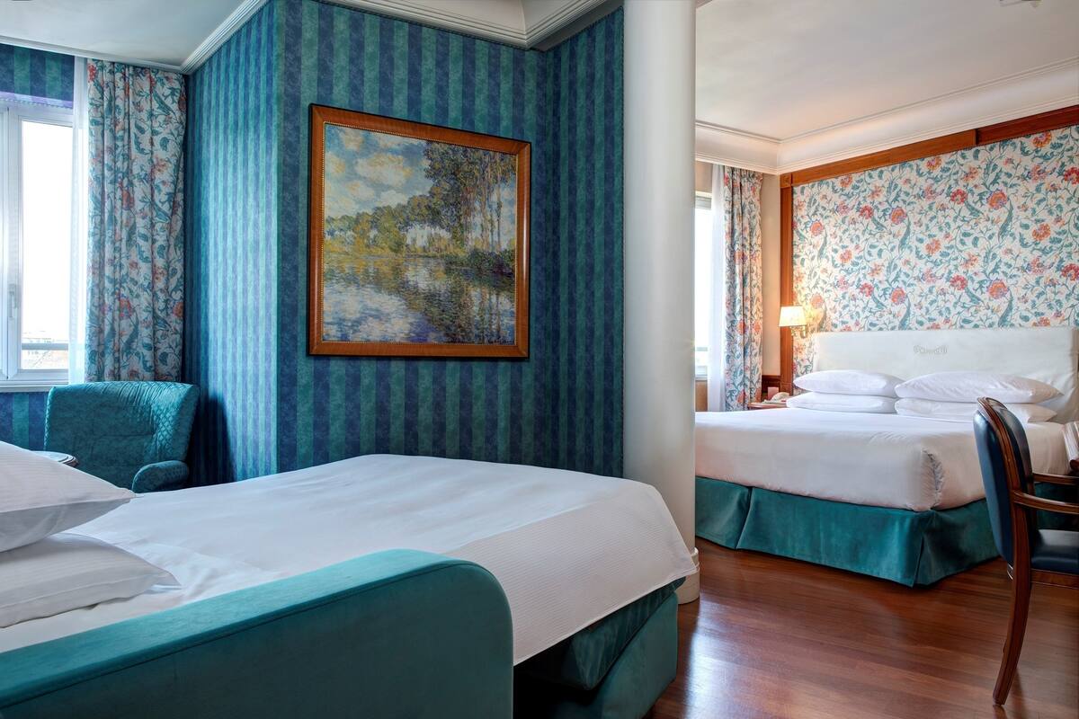 A hotel room with two beds, a large painting, and striped wallpaper.