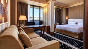 Een hotelkamer met een bank, een bureau met lamp, een bed en uitzicht op de stad.