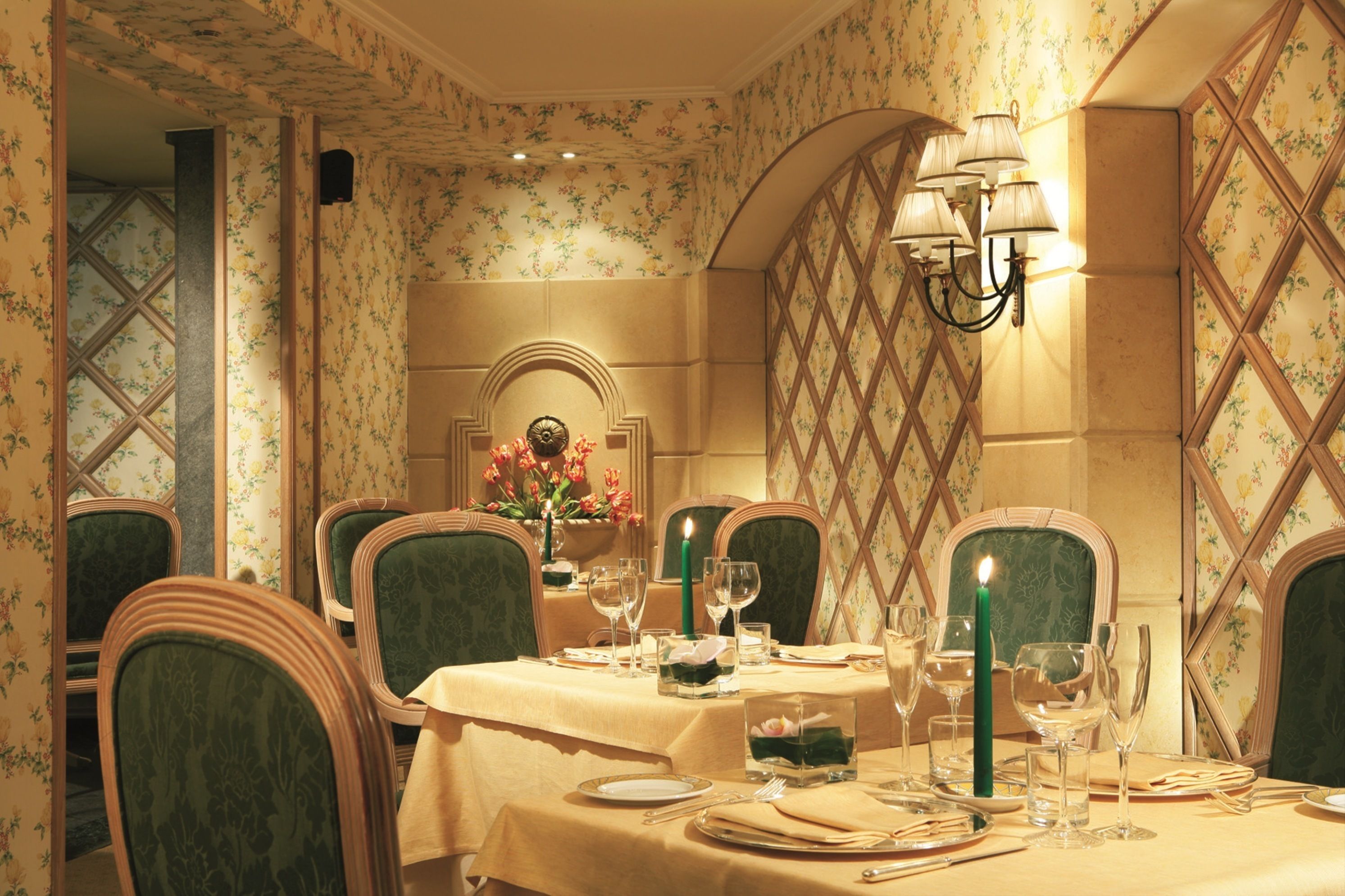 A dining room with a table set for four, floral wallpaper, and a chandelier.