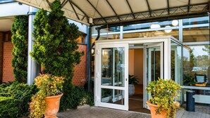 Een hotelingang met een overdekt terras, glazen deuren en potplanten.