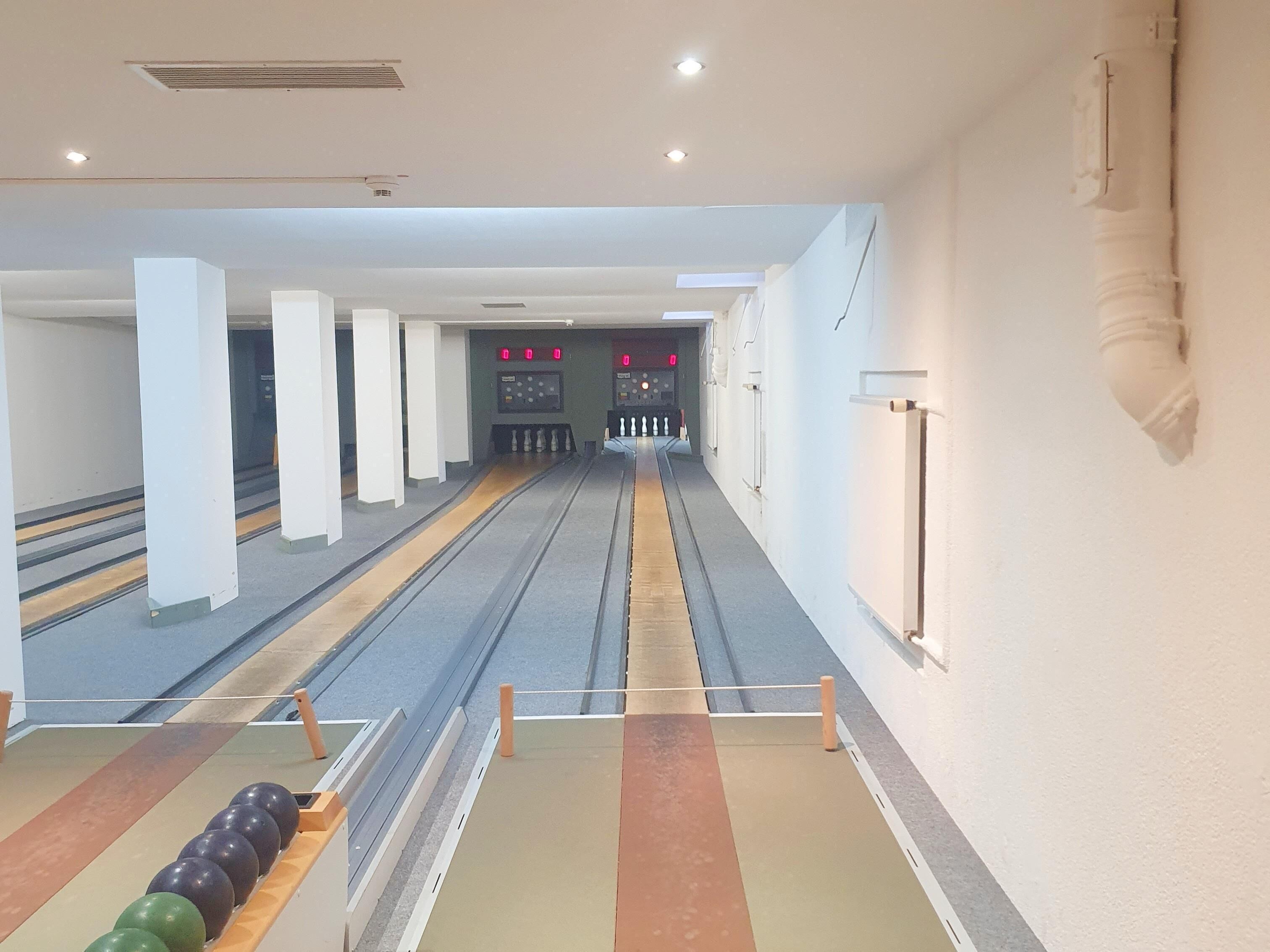 Une salle de bowling avec des pistes, un présentoir à boules et un tableau d’affichage des scores.
